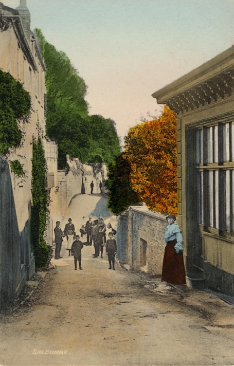 Around 1900  Cliff Road, Salcombe, at Baker*s Well, view from the southern end. Cliff House is at rear left. Children standing in road, young lady in doorway of house on right.