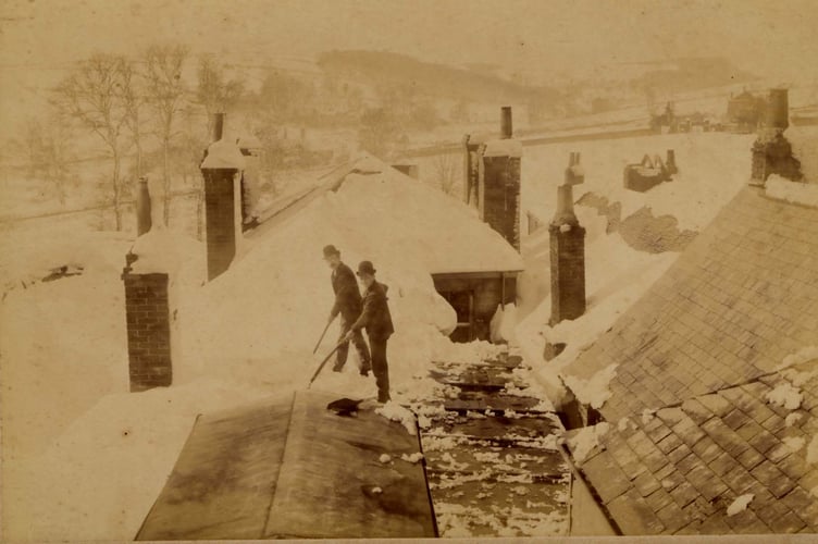 March 1891. Two men clearing snow from a roof on the west side of Fore Street, Kingsbridge, after the blizzard.  Possibly the workhouse on the far right.