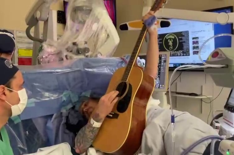 Paul Welsh-Dalton, playing guitar whilst having a tumour removed. // A man had a tumour the size of a kiwi removed from his brain all whilst awake and playing the guitar. Paul Welsh-Dalton underwent surgery to remove his oligodendroglioma a rare type of malignant brain tumour on March 28. A sudden seizure at home after having suffered with aphasia and headaches meant Paul was admitted to hospital three weeks prior where doctors discovered the mass. During the five-hour craniotomy surgeons removed 98 per cent of the four-centimetre tumour with Paul playing music on his guitar to help gauge if Pauls brains abilities were being compromised.