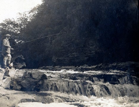 Sidney Dent fishing from bank of river by small rapids